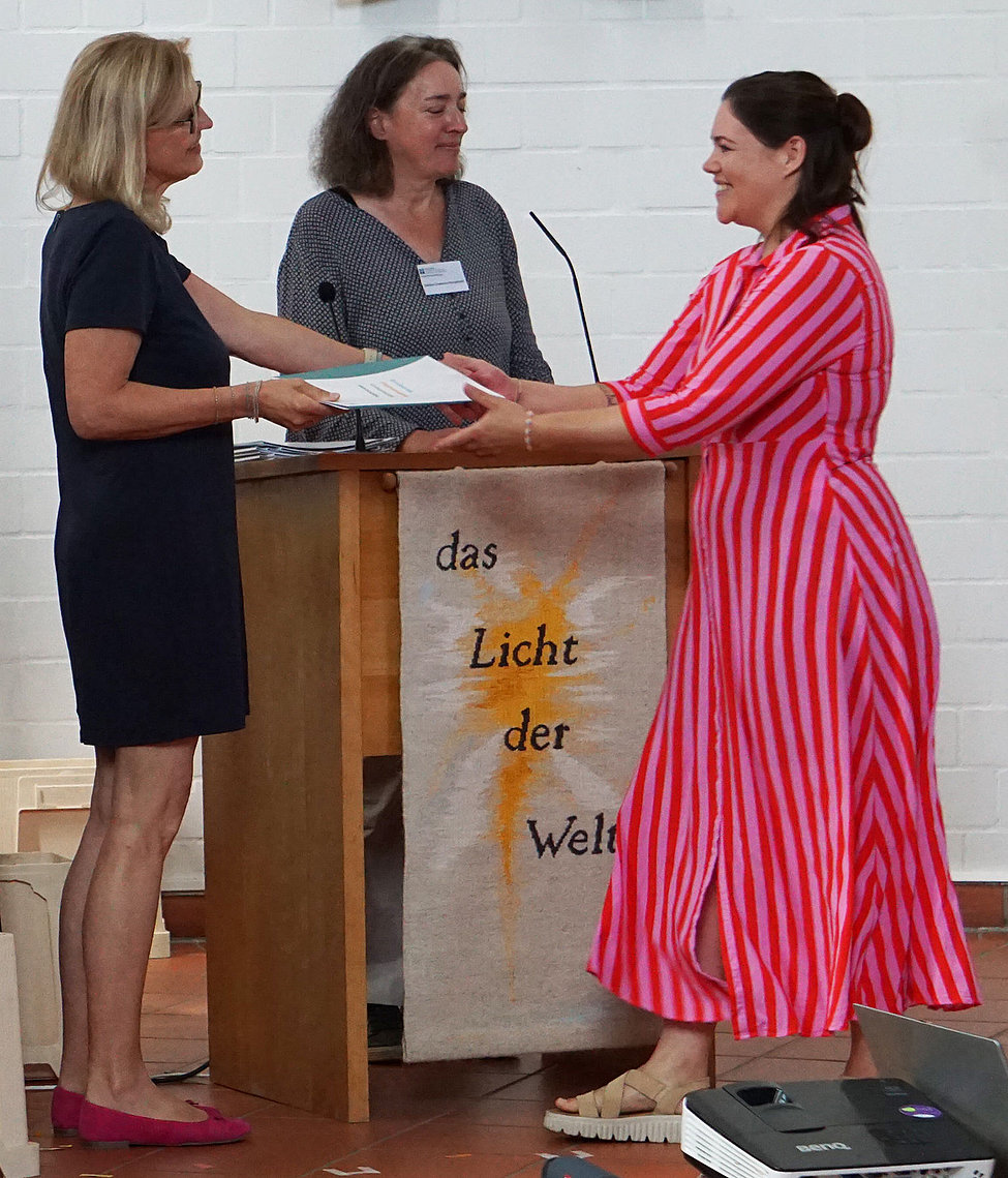 Zwei Frauen überreichen bei Abschlussfeier ein Dokument Banner das Licht der Welt