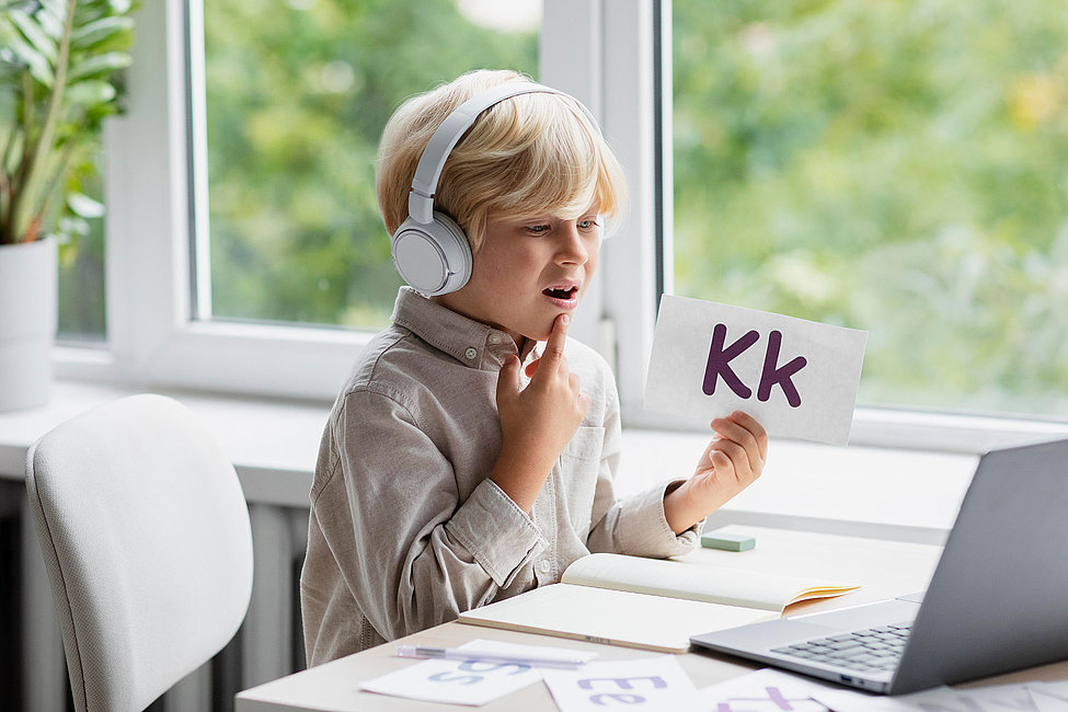 Kind mit Kopfhörern hält Karte Kk beim Sprechtraining